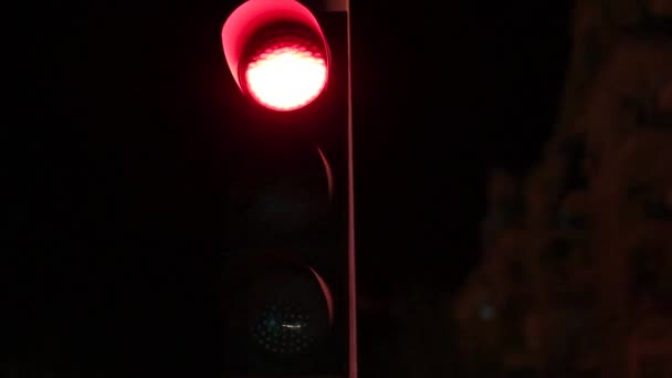 Stop light slowly changing from red to yellow to green light at night with buildings in the background.