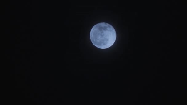 Pleine lune haute sur le ciel noir nocturne avec des nuages passant devant elle .