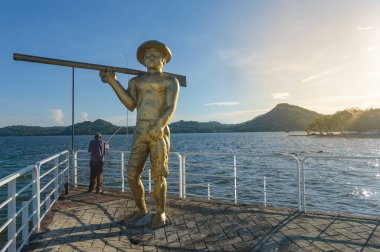 CATEMACO, VERACRUZ - MEXICO, 19 Haziran 2018: Catemaco Gölü kıyısında bir balıkçının tarihi heykelinin yanında balık tutan yaşlı adam
