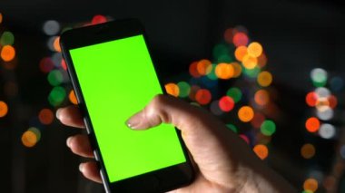 Kadının elinde yeşil ekranlı ve parşömenli bir akıllı telefon var. El ve telefon yakın plan.
