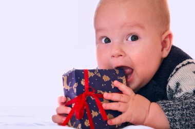 Sevimli beş aylık bebek bir hediye kutusu tutuyor ve onu ısırıyor. Yetenekli komik çocuk beyaz arka plandaki kameraya bakıyor..