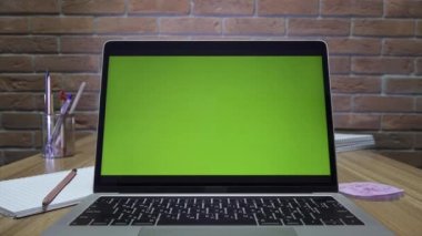 Ofisteki masasında yeşil ekranlı dizüstü bilgisayar. Dolly zoom çekimi. Çatı katı tarzı ofis. Arka planda tuğla bir duvar var..