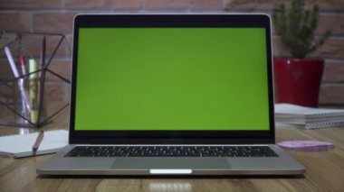 Ofisteki masasında yeşil ekranlı dizüstü bilgisayar. Dolly zoom çekimi. Çatı katı tarzı ofis. Arka planda tuğla bir duvar var..