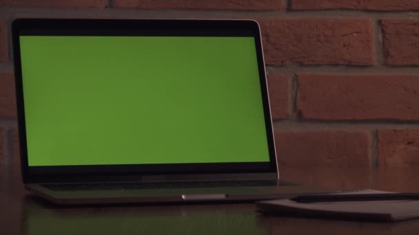 コンテンツ用の緑色のスクリーンノートパソコン レンガの壁を背景にオフィスのテーブル上のコンピュータ — ストック動画