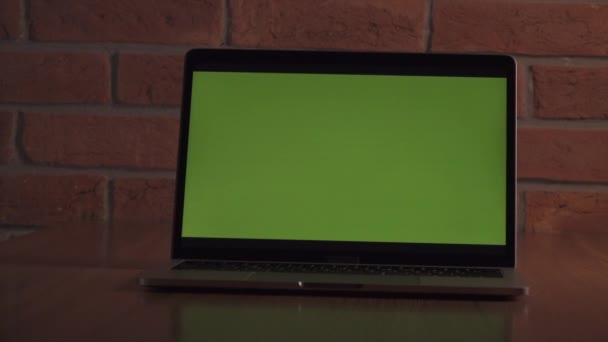 コンテンツ用の緑色のスクリーンノートパソコン レンガの壁を背景にオフィスのテーブルの上のコンピュータ カメラが動く — ストック動画
