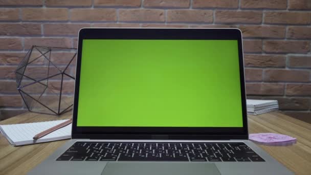 オフィスの机の上に緑の画面を持つノートパソコン ドリーズーム撮影 ロフトスタイルのオフィス 背景にレンガの壁があります — ストック動画