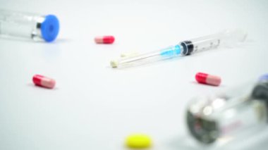Haplar ve vitaminler şırınga ve ilaç şişelerine düşer. Ağır çekim. Beyaz arka planda tabletler, vitaminler, ilaç şişeleri ve şırıngalar