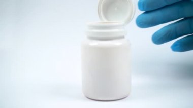 Elindeki tıbbi eldiven vitamin şişesini itiyor. Sarı haplar şişeden yavaş çekimde düşer. C vitamini hapları