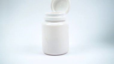 Elindeki tıbbi eldiven vitamin şişesini itiyor. Sarı haplar şişeden yavaş çekimde düşer. C vitamini hapları