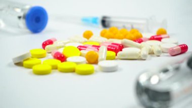 Renkli tabletler, haplar, ilaç şişesi ve beyaz arka planda şırınga. Tıbbi hazırlıklar. 4 bin. Kamera hareket ediyor