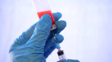 Hastane ve ilaç. Doktor şırıngayı şişeden kırmızı sıvıyla dolduruyor. Doktorun elinde mavi eldiven var. Şırıngayı doldur.