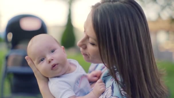 母亲带着一个孩子在公园外面 年轻的黑发女人抱着四个月大的男婴 后面是一个婴儿车 慢动作 100 Fps — 图库视频影像