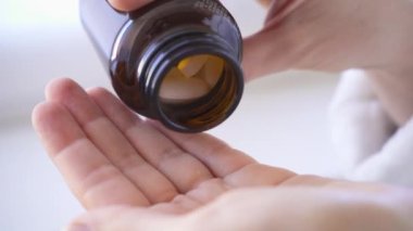 Kadın şişeden avuç içine hap döküyor. Hapları yakın planda tut. Haplar ağır çekimde şişeden dökülüyor.