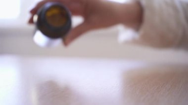 Masanın üzerine beyaz haplar döken bir kadının yakın çekimi. Haplar yavaş çekimde düşer..