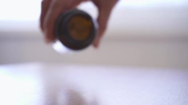 Masanın üzerine beyaz haplar döken bir kadının yakın çekimi. Haplar yavaş çekimde düşer..