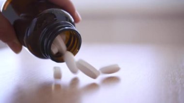 Masaya cam şişeden düşen 4K haplar. Kadın elinin yakın plan çekimi masaya beyaz haplar döker.