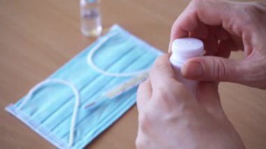 Yakın plan haplar el altında. Kadın avucunun içine beyaz bir şişeden iki tablet dolduruyor.