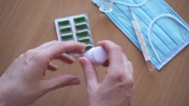 Yakın plan haplar el altında. Kadın avucunun içine beyaz bir şişeden iki tablet dolduruyor.