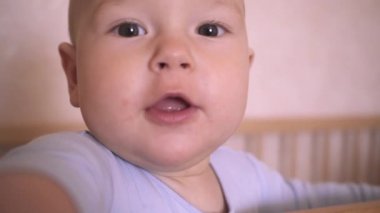 Şirin Bebek Yakın Çekimi. Çocuk kameraya bakar ve elini uzatır. Dokuz aylık erkek bebek, çocuk odasında bir beşikte