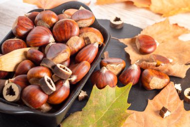 Kurumuş portakal yapraklarıyla dolu bir kase dolusu kestane. 