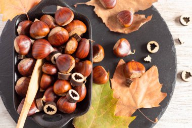 Kurumuş portakal yapraklarıyla dolu bir kase dolusu kestane. 