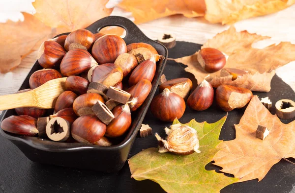 Kurumuş portakal yapraklarıyla dolu bir kase dolusu kestane. 