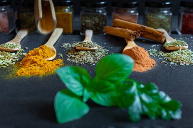 Farklı renklerde baharatlar ve otlar. Tahta kaşıklarda siyah tahta taşlarda.