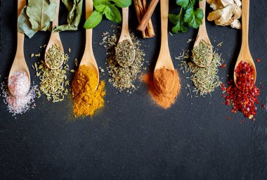 Farklı renklerde baharatlar ve otlar. Tahta kaşıklarda siyah tahta taşlarda.