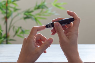 Glikoz seviyesini dijital glukometreyle kontrol etmek için kan örneği alan kadın.