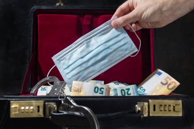 Beyaz bir adam, kelepçeli ve banknotlu güvenlik çantasının içine yüz maskesi sokuyor.