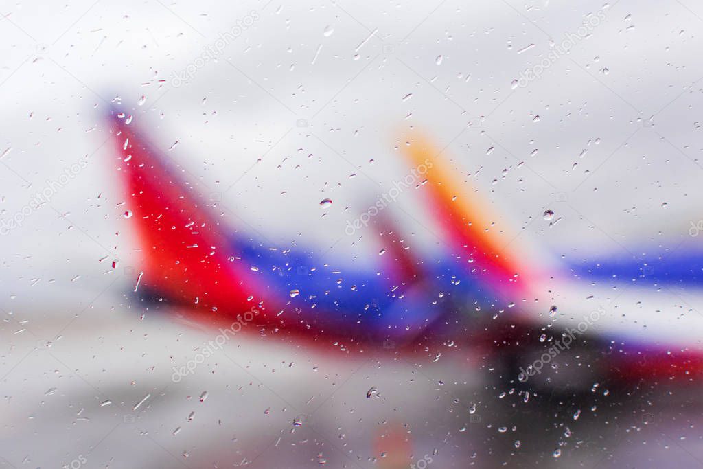 Defocused view on airplanes through airport terminal window with rain drops