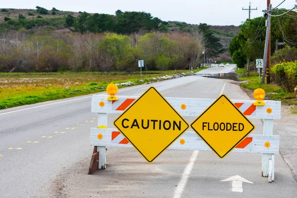 Caution and Flooded warning signs on barricade installed across two-way street to warn drivers about flooded highway