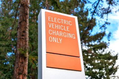 Elektrikli araç arka planda bulanık yeşil ağaçlar olan sadece uyarı işareti yüklüyor. Elektrikli araç şarj istasyonu yakınındaki Ev araçları için belirlenmiş park yeri