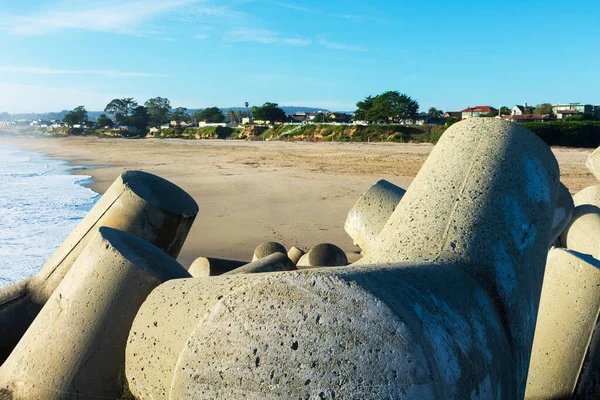 Reinforced concrete dolosse protecting breakwater jetty of Santa Cruz Harbor. Background sandy beach and blue sky