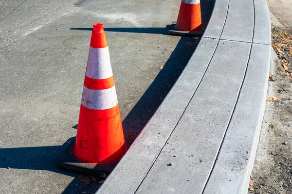 Red traffic cones protect newly build concrete curb. Road pavement renewal. Parking lot or road infrastructure repair — Stock Photo, Image