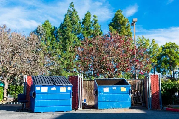 Dva odpadové kontejnery s modrým odpadem používané pro komerční a obytné odpadky. Zelené stromy. Modrá obloha. — Stock fotografie