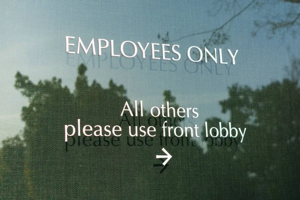 Employees only sign on the glass door leading to office directs company customers and visitors to front lobby