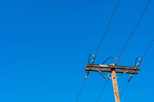 High voltage wooden utility pole, column or post with parallel single-circuit lines in the blue sky.