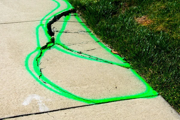 Marked sidewalk trip and fall hazard on cracked concrete slab. The walkway requires inspection and repair to prevent accident legal liability for pedestrian injury