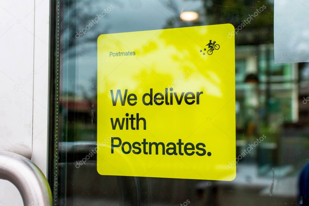 Close up. A yellow sticker decal on a restaurant door advertising delivery service available through Postmates goods delivery service - San Francisco, California, USA - 2020
