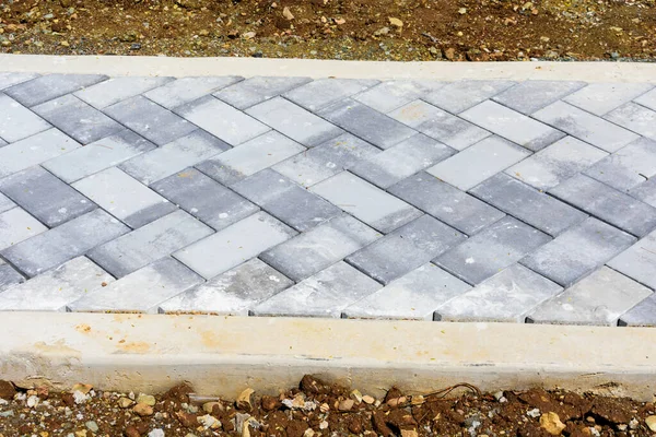 Pedestrian walkway construction. Brick pavers set up in a herringbone pattern between new concrete curbs surrounded by freshly dug brown earth