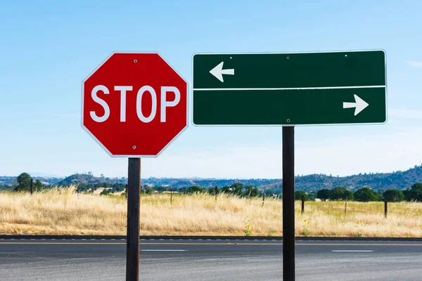 白の方向の矢印と8面の赤のStop記号と長方形の緑のガイド道路標識 背景黄金の草 水平線上の山の風景 — ストック写真
