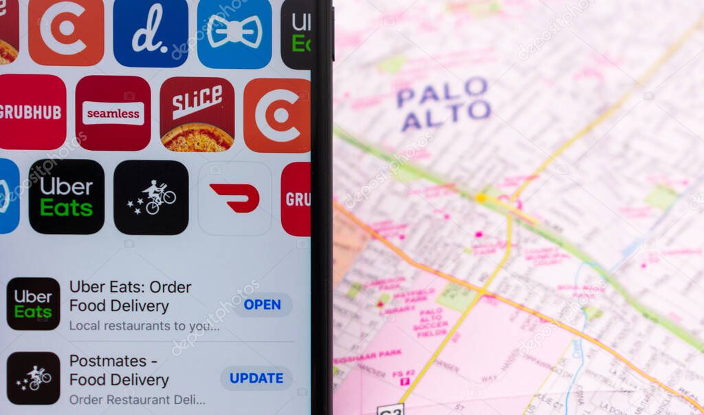Mobile app icons of competing food delivery services on a smartphone: DoorDash, Grubhub, Uber Eats, delivery.com, Seamless, Postmates. Background blurred map - San Jose, CA, USA - 2020
