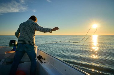 Genç adam teknede balık tutuyor. 