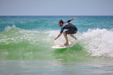 Genç sakallı adam denizde sörf yapıyor. 