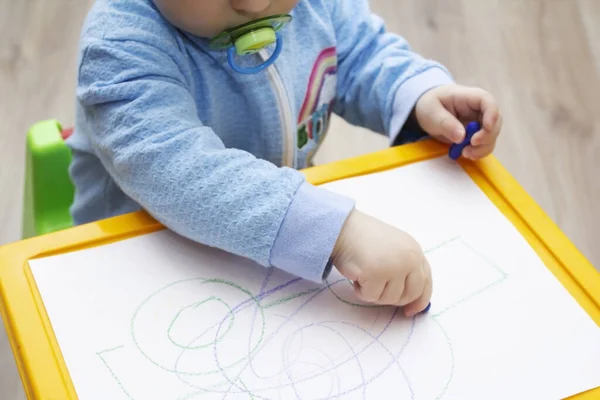 Close-up of a small child's hands draw with wax crayons. the child sits at the table and draws, the workplace of the baby