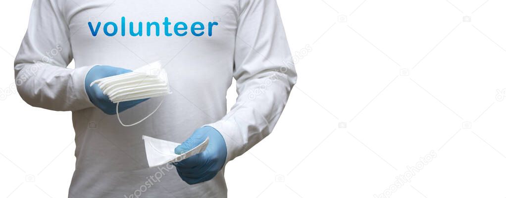 A volunteer wearing gloves and a mask holds a stack of medical masks in his hand. The concept is protection against coronavirus, covid-19 and influenza. Template with space for text.