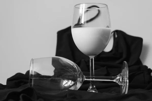 A glass with a white drink stands on a small black dress thrown on the table. The empty glass lies nearby.