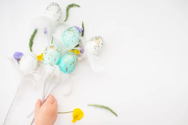 Пасхальні біло-блакитні яйця в золотій плямі на паличках на плетеному фоні з дитячою рукою. Великодня концепція подарунка . — стокове фото