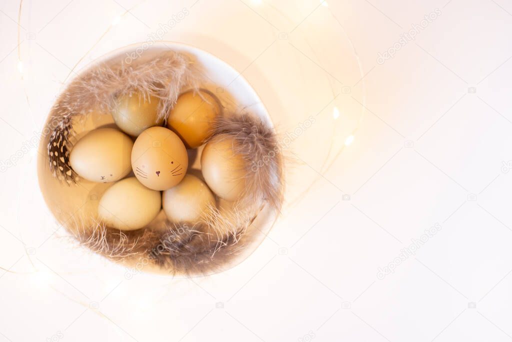 Stylish Easter festive eggs in natural color on a Black background with garlands with feathers in wihte bowl.